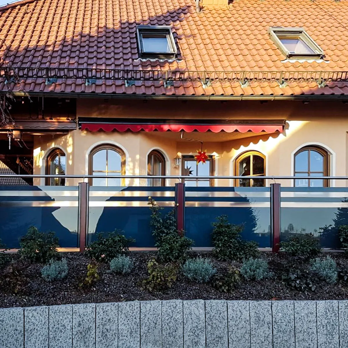 Pfostengeländer mit Glas vor einem Haus mit Garten