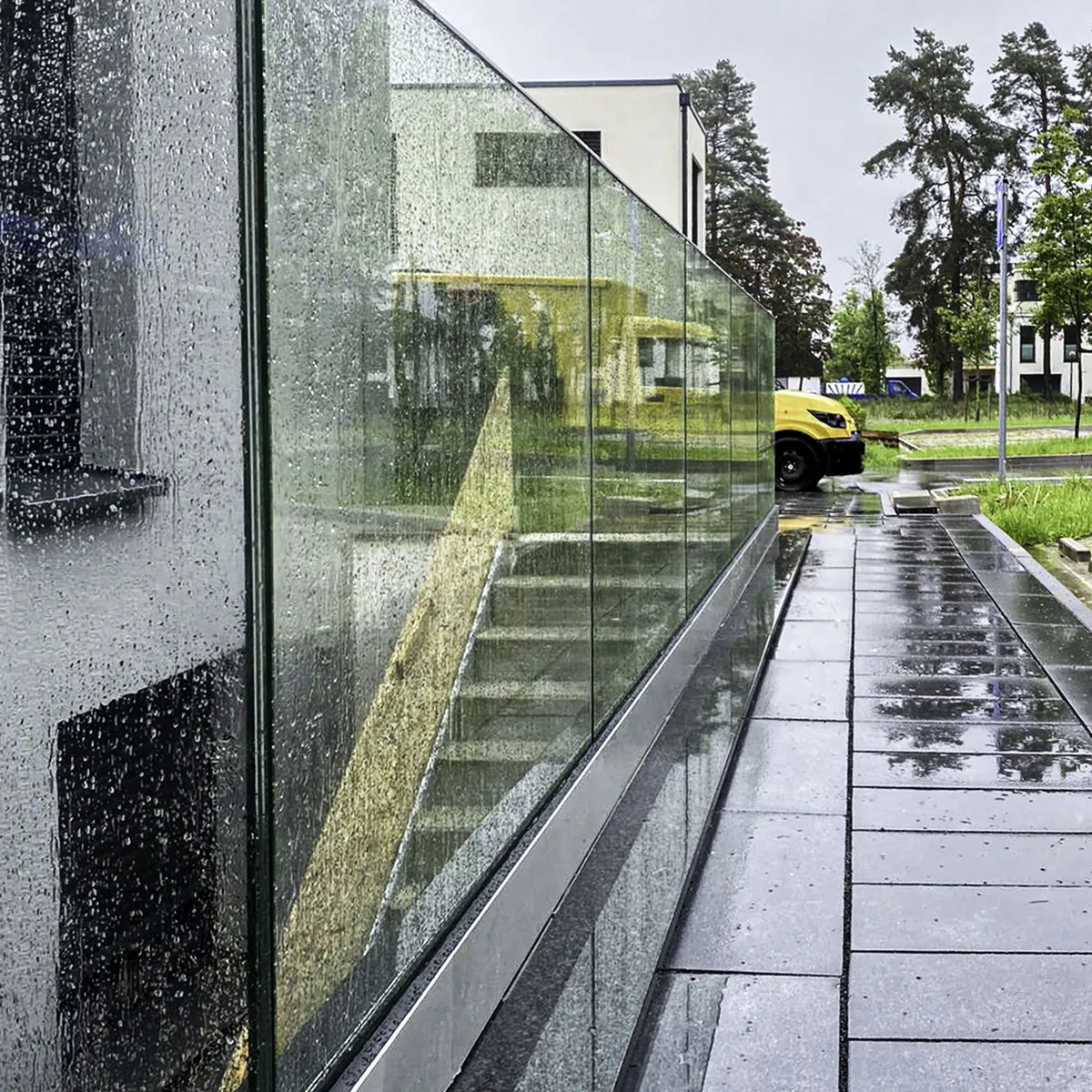 Glasgeländer aus VSG-Glas mit Regentropfen an einem Weg entlang der Hauswand
