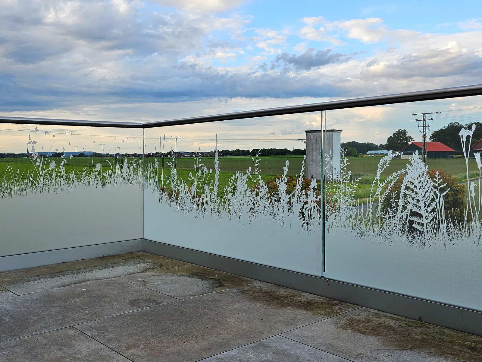 Dachterrasse mit Glasgeländer und Gräsermotiv vor weiten Feldern