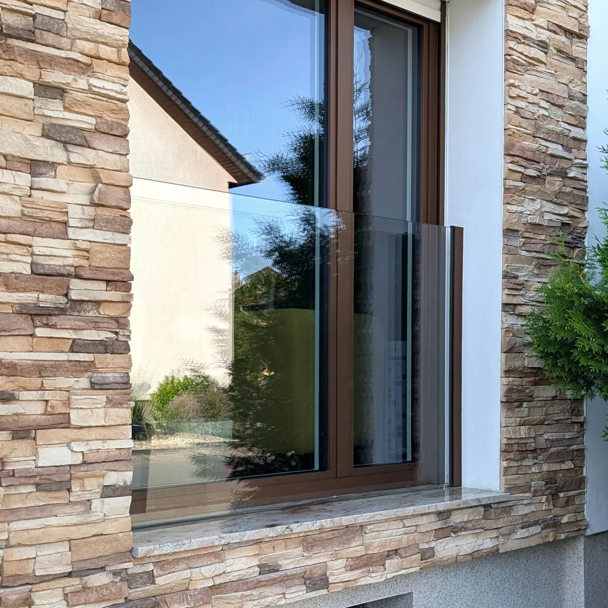Französischer Balkon aus Glas vor einem bodentiefen Fenster in einer Natursteinfassade