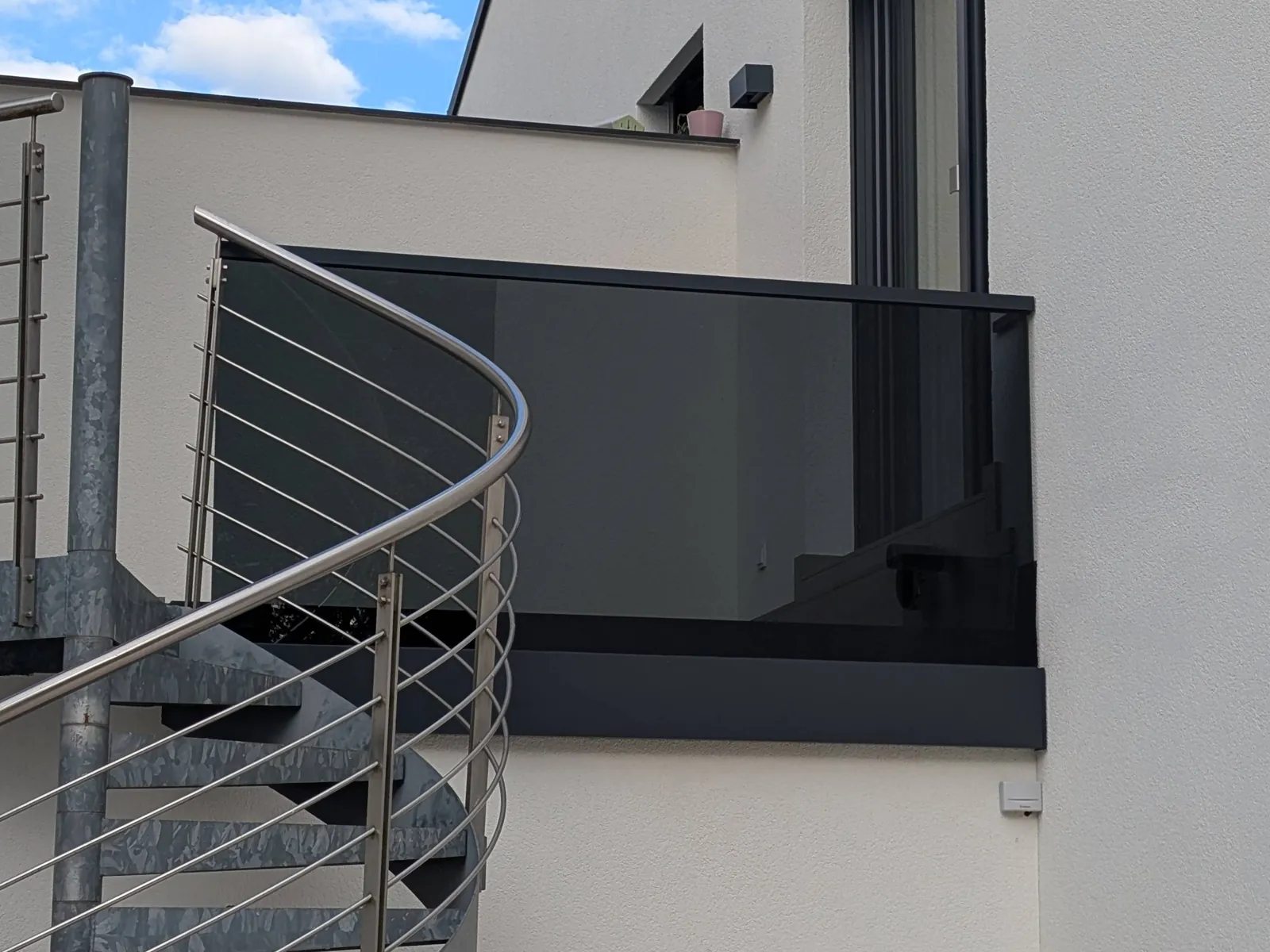 Balkon mit Glasgeländer aus Grauglas neben einer Wendeltreppe